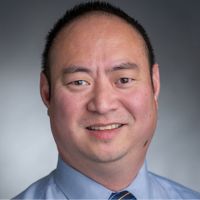 Portrait of a researcher in a dress shirt and tie, smiling against a neutral background.