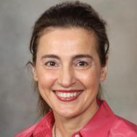 Portrait of a smiling researcher with long hair wearing a pink blouse against a neutral background.