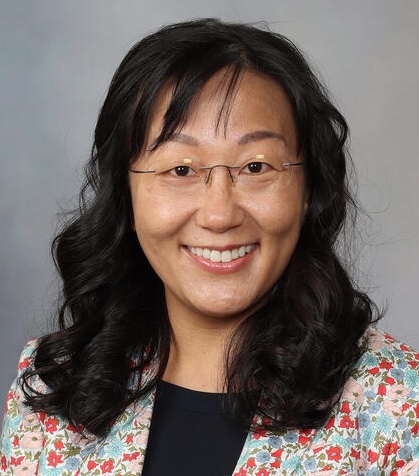 Portrait of a smiling researcher with curly hair and glasses, wearing a floral blazer.