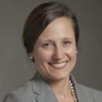 Portrait of a smiling professional woman in a gray blazer with pearls.