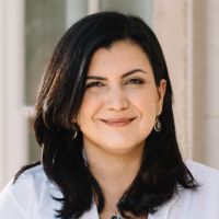 Portrait of a researcher with dark hair and a white shirt, smiling outdoors.