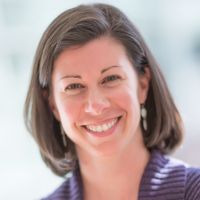 Portrait of a smiling woman with shoulder-length hair, wearing a purple sweater, likely a researcher.