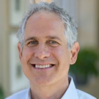Portrait of a smiling researcher with gray hair and a light blue shirt.