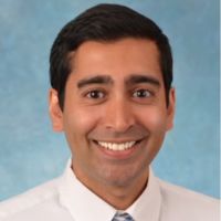 Portrait of a smiling male researcher in a white shirt and tie against a blue background.