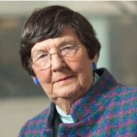 Portrait of a senior woman with short hair, wearing glasses and a colorful jacket.