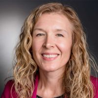 Portrait of a smiling woman with curly hair, wearing a pink blazer.
