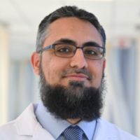 Portrait of a researcher in a lab coat with glasses and a beard.