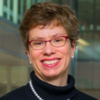 Portrait of a smiling woman with short hair, wearing glasses and a dark sweater.