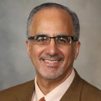 Portrait of a researcher in a suit and glasses smiling against a neutral background.