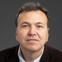 Portrait of a researcher with short dark hair, wearing a black jacket and a collared shirt.