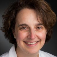 Portrait of a smiling researcher with curly hair, wearing a white lab coat.