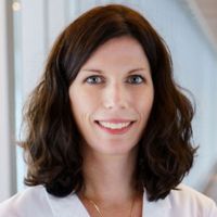 Portrait of a researcher in a lab coat smiling at the camera.